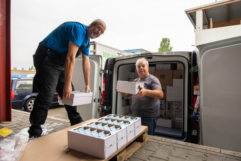 2 Tafel-Helfer laden Pflanzenmilch in einen Transporter.