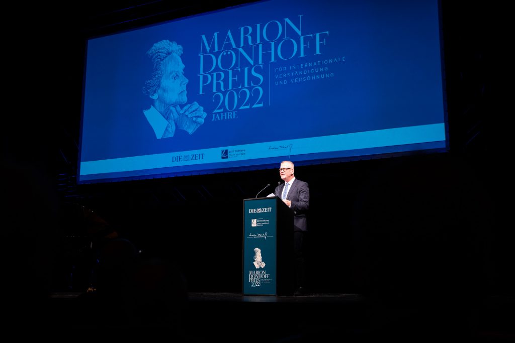 Jochen Brühl steht auf einer Bühne am Rednerpult. Hinter ihm ist eingeblndet: "Marion Dönhoff Preis 2022".
