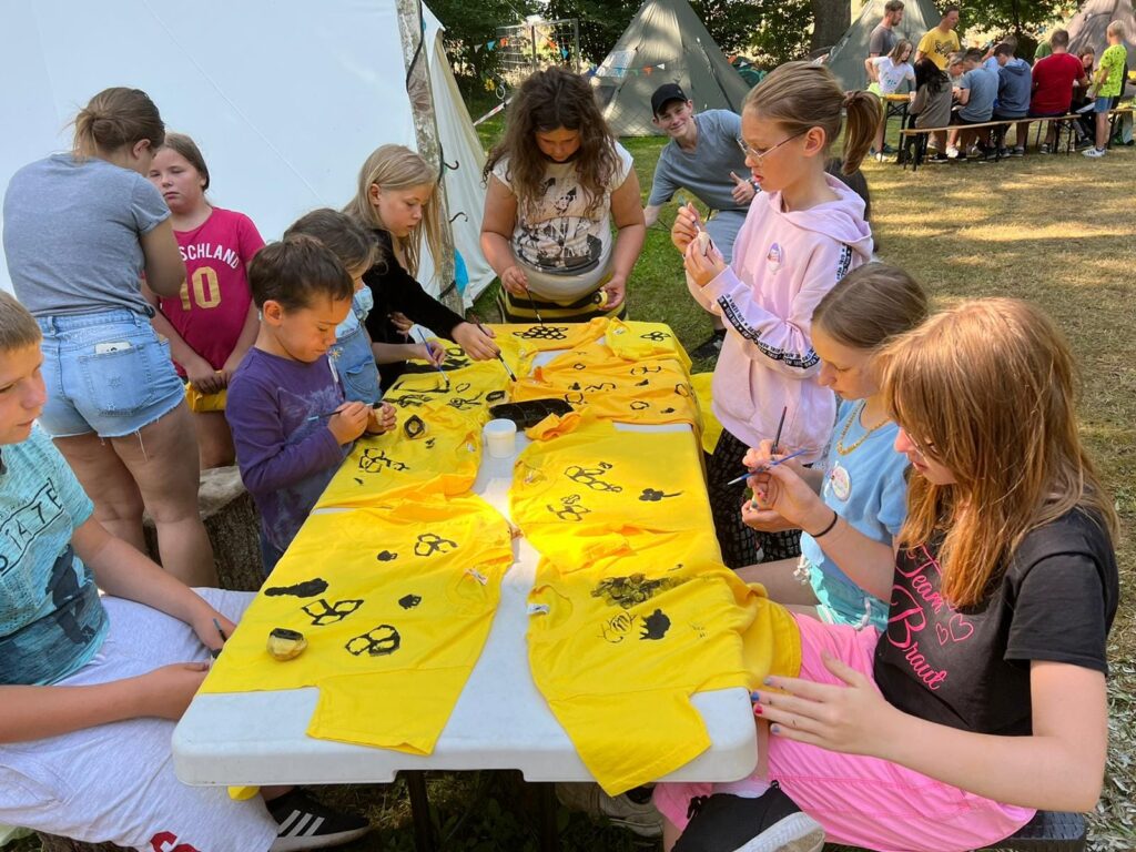Kinder an einem Tisch bemalen T-Shirts mit Bienen