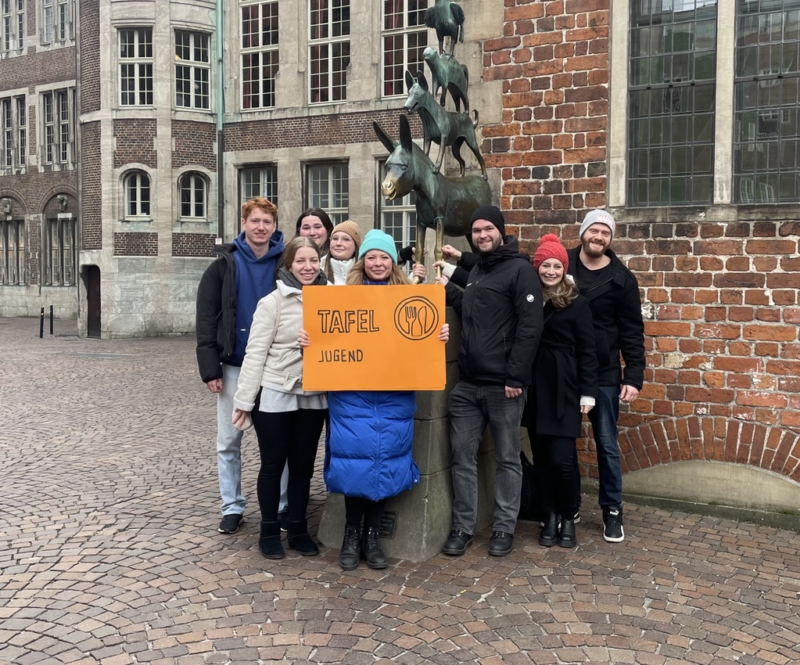 Junge Tafel-Aktive poieren vor dem Denkmal der Bremer Stadtmusikanten