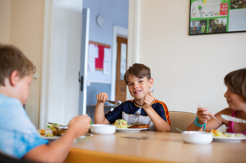 Drei Kinder sitzen gemeinsam am Tisch und essen ihre selbstgemachte Mahlzeit