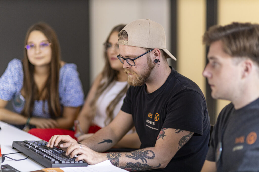 Ein Tafel-Aktiver tippt auf einer Computertastatur. Neben ihm sitzen 3 weitere Ehrenamtliche, die auf den Computerbildschirm schauen.