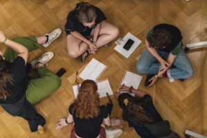 Vogelperspektive auf 5 Tafel-Aktive, die auf dem Boden sitzen und sich Notizen in einem Workshop machen.