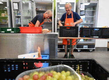 Zwei Tafel-Helfer sortieren Kühlware in Kühlschränke ein. Im Vordergrund sind Weintrauben zu sehen.