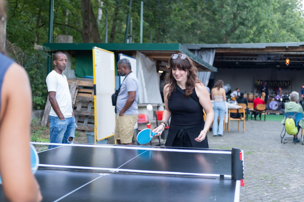 Die Bühne ist im Hintergrund zu sehen und vorn spielt eine Frau Tischtennis. 