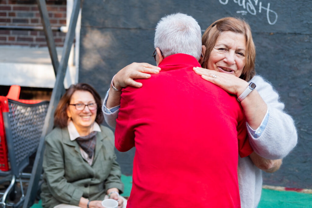 Ein Mann umarmt eine Frau, eine andere Frau lacht im Hintergrund. 