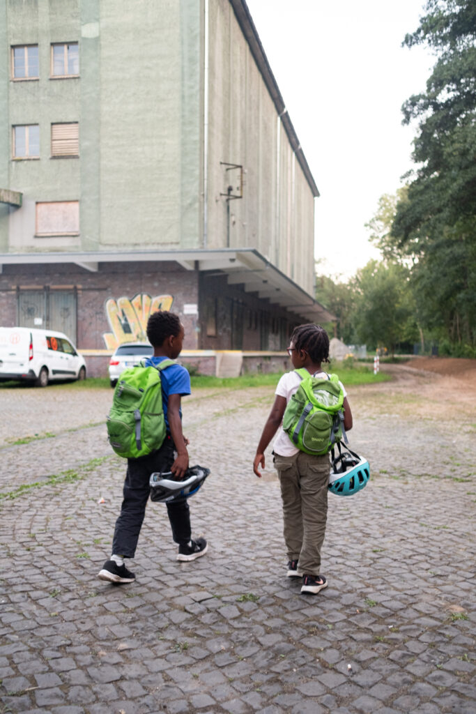 Zwei Kinder mit Rucksäcken und Fahrradhelmen gehen in Richtung Ausgang. 