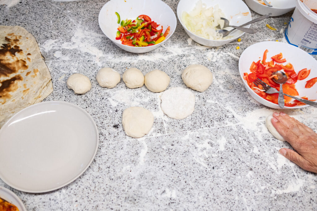 Teig, Gemüse und Käse stehen bereit, um die Pizza zuzubereiten. 