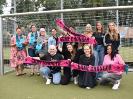 12 Frauen stehen in einem Tor und lächeln in die Kamera. Sie halten Schals mit der Aufschrift "Game Changer".