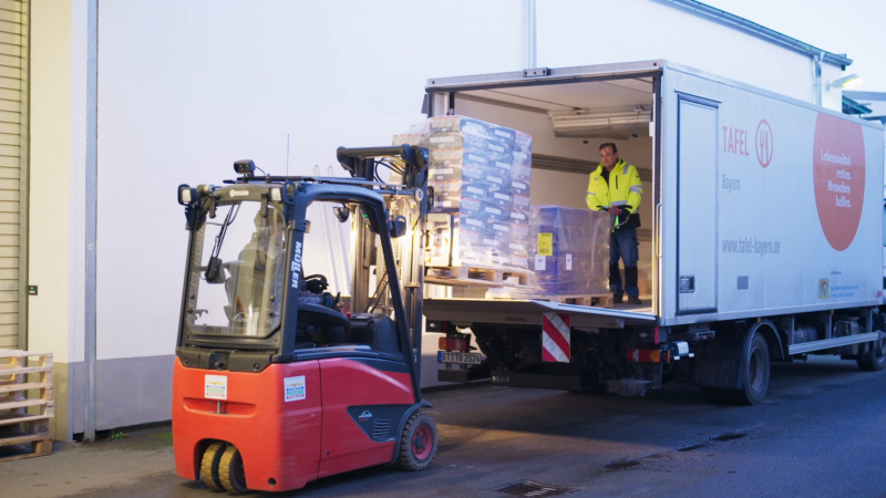 2 Tafel-Helfer laden Paletten mit haltbaren Lebensmittel aus einem Lkw aus.