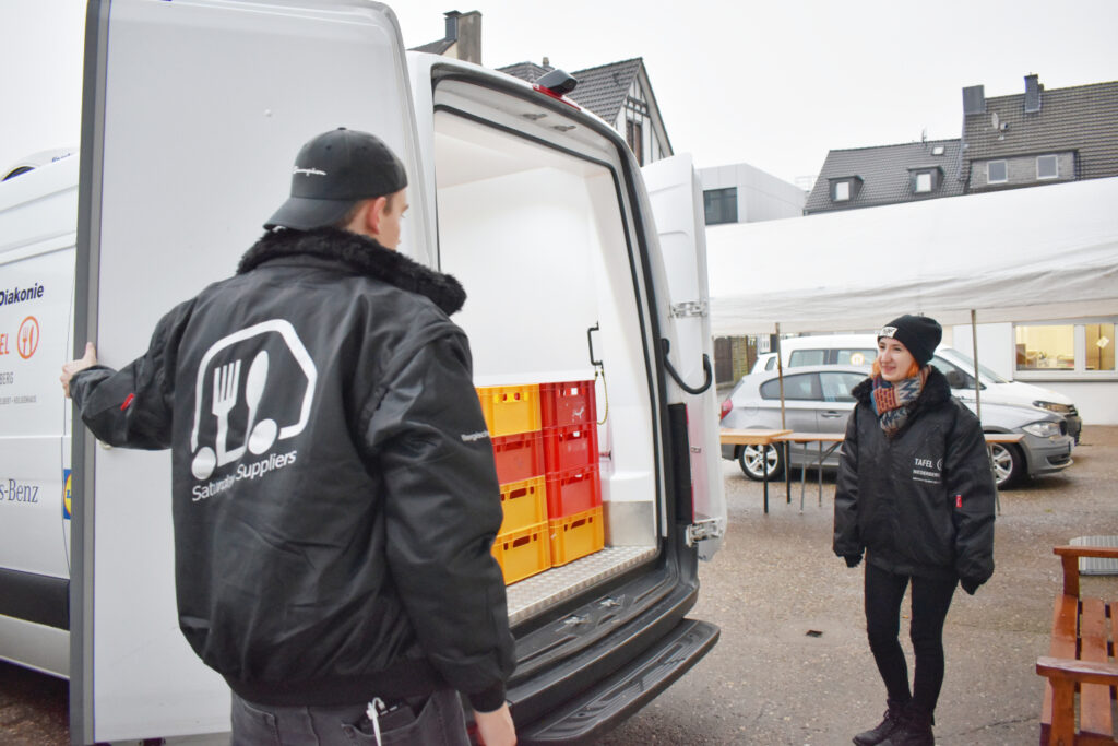 2 Tafel-Helfer:innen der Saturday Suppliers beladen ein Fahrzeug.