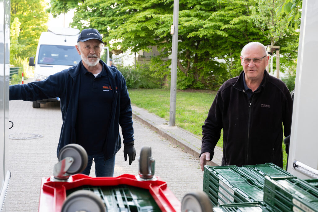2 Tafel-Helfer beladen ein Fahrzeug mit leeren Kisten, bevor sie losfahren.