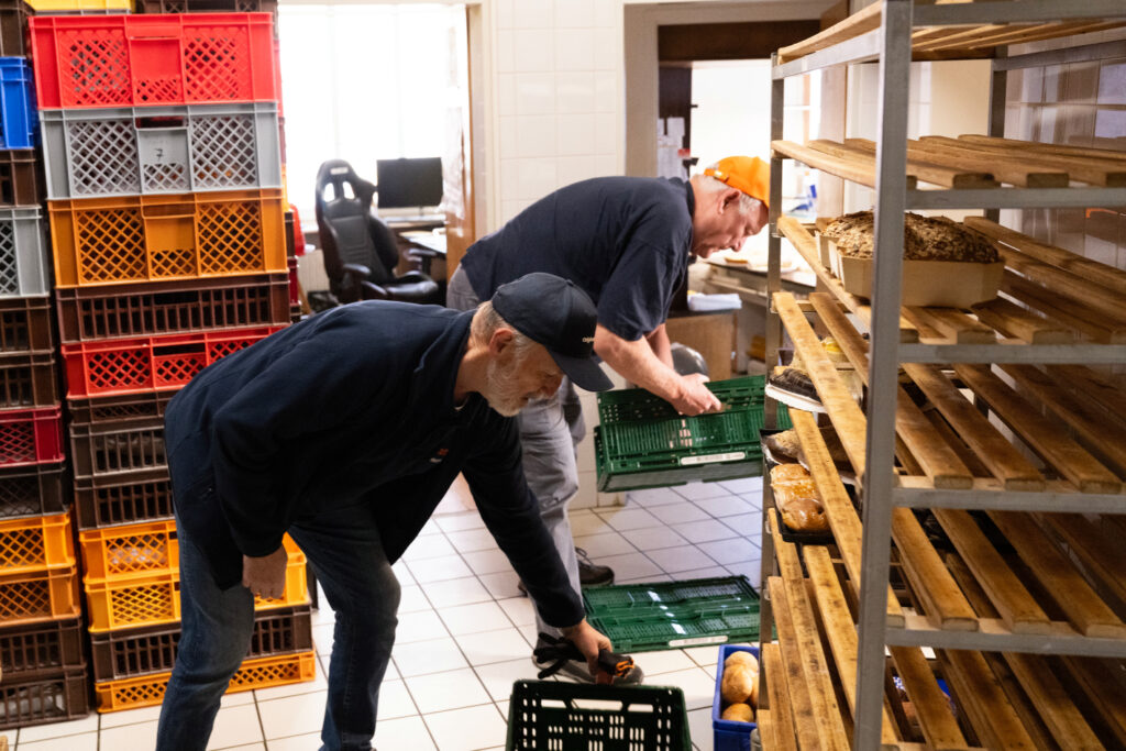 2 Tafel-Helfer legen gespendete Brote in einer Bäckerei in ihre Kisten.